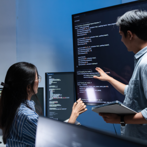 A man and a woman analyzing code in a poor light room on 2 screens