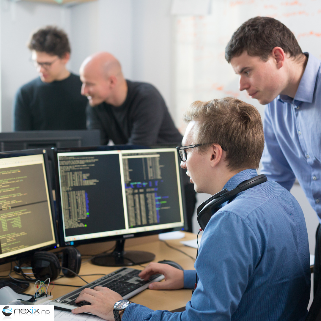 2 men in the front looking at 2 screens of computer